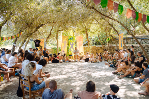 Un grande cerchio di persone sedute all'ombra degli alberi