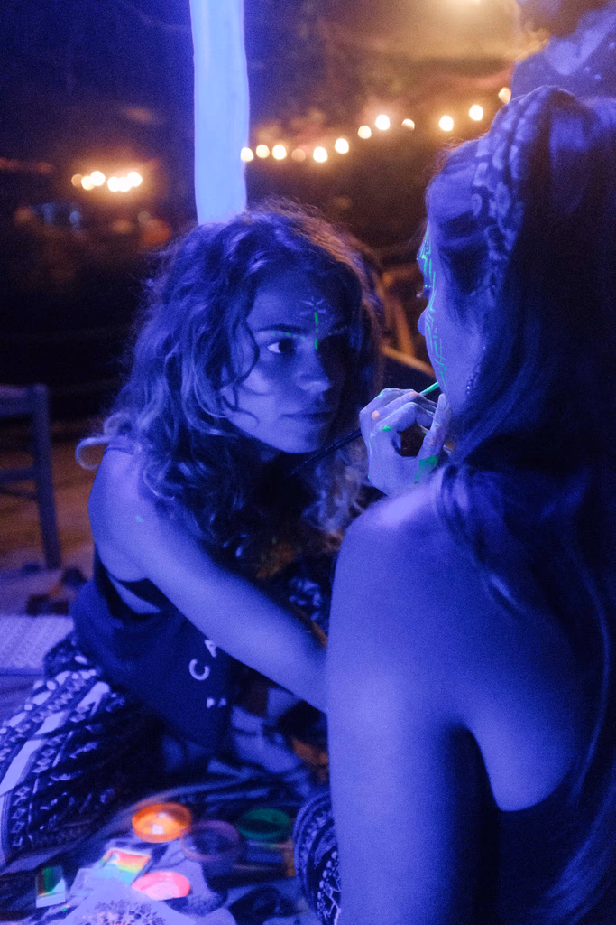 Due persone che si dipingono il viso con i colori fluo