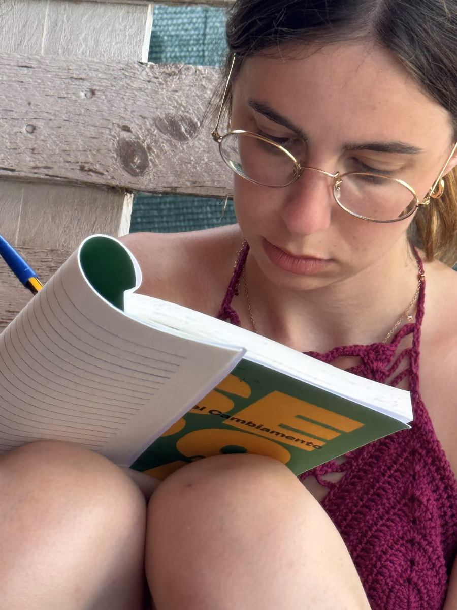 Una ragazza con gli occhiali, seduta con le ginocchia al petto, scrive con la penna sul diario Sepofà