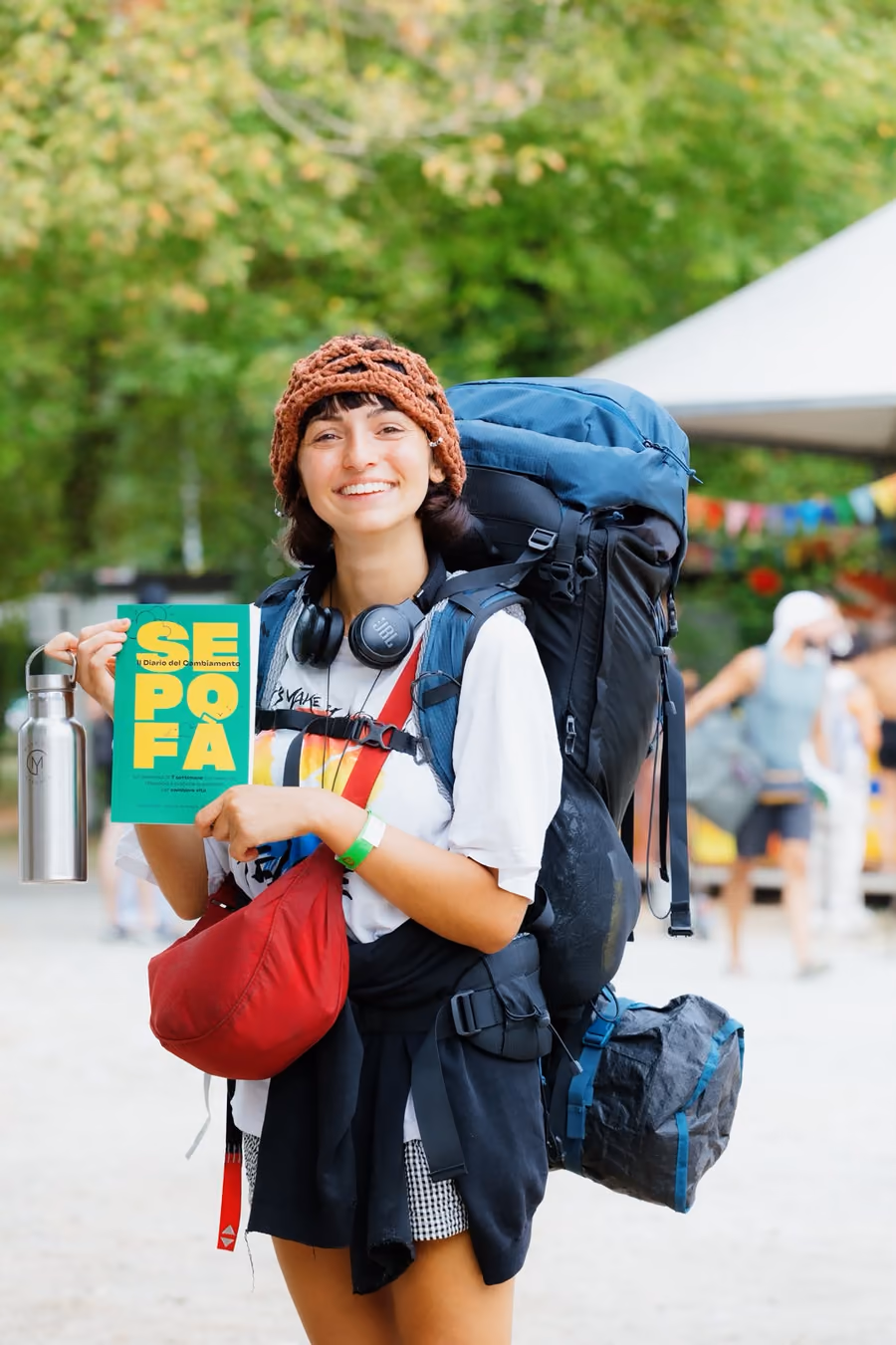 Una ragazza con un grande zaino da viaggio in spalla mostra sorridendo il Sepofà